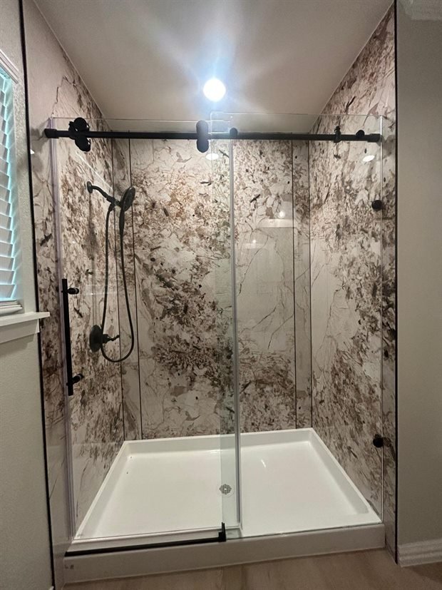 Completed walk-in shower with marble-pattern surround, sliding glass doors and matte black fixtures