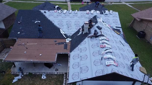Drone view of a roof half stripped to underlayment and half still carrying its old shingles