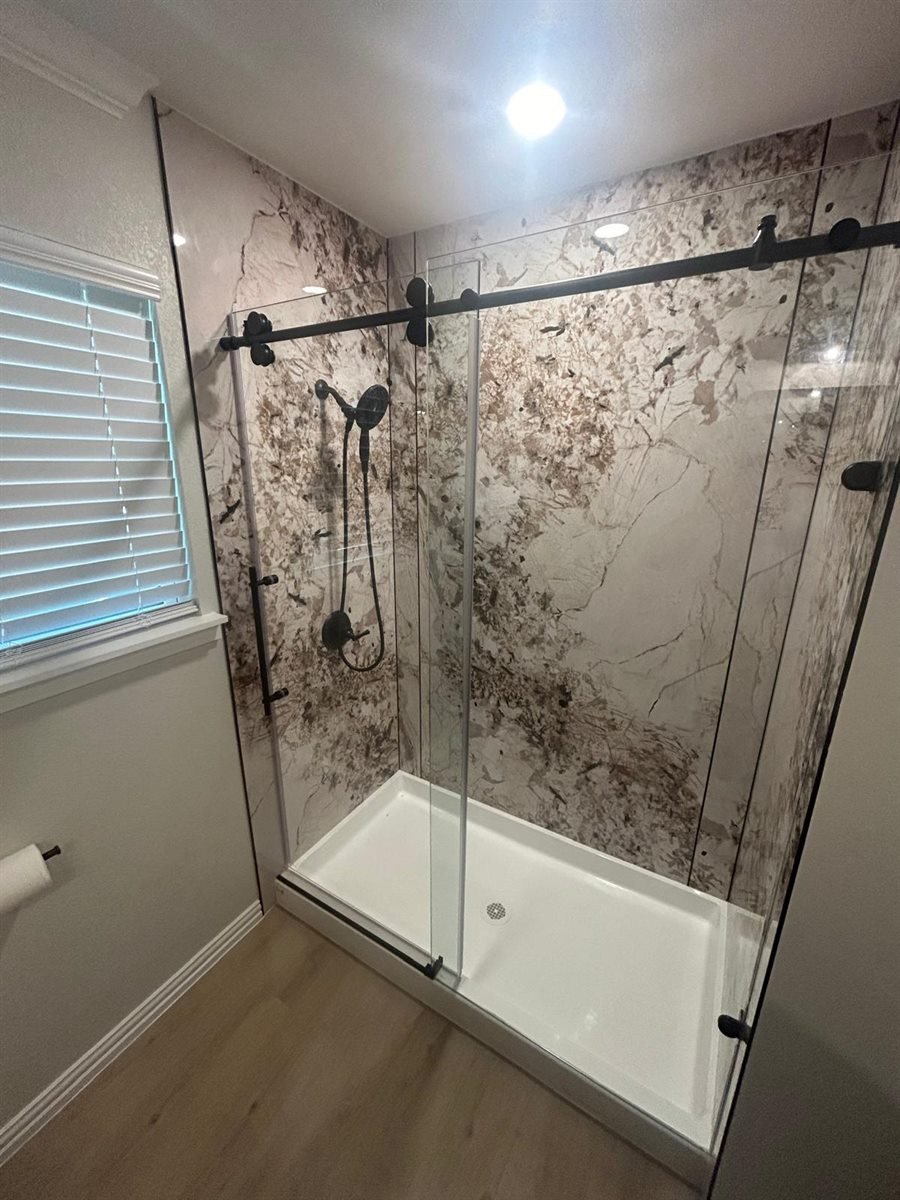 Completed bathroom remodel with a marble-pattern walk-in shower, frameless glass doors and matte black fixtures