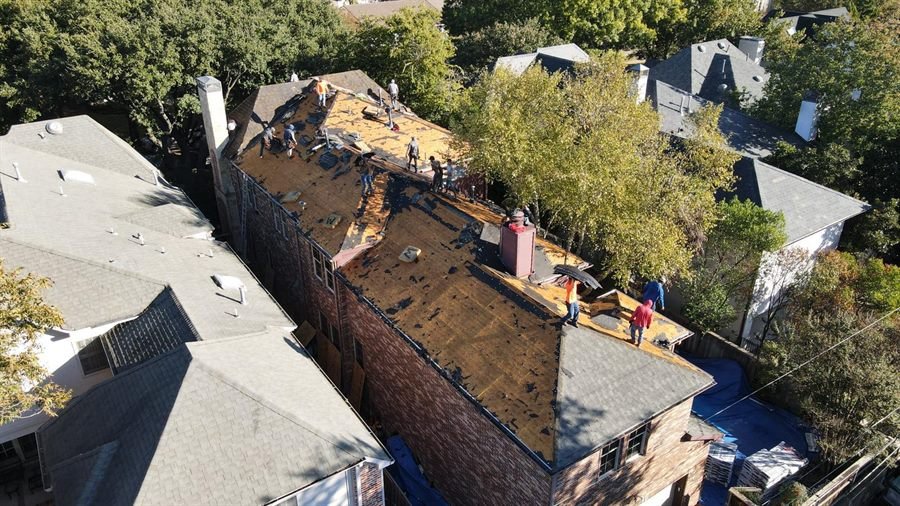 Drone view of a large two-storey home stripped back to bare roof decking with a full crew working